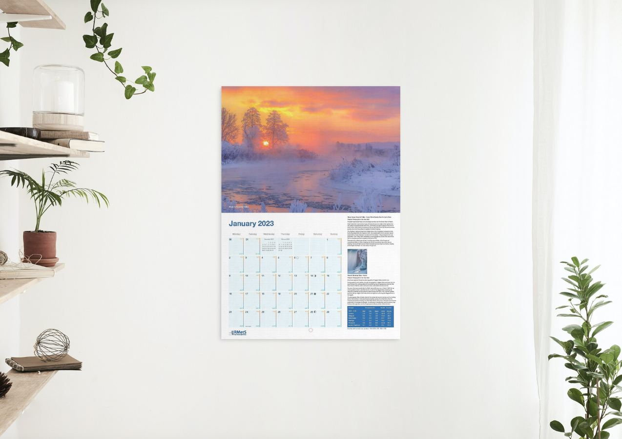 January's page showing a colourful frosty river scene with the calendar grid below. It is shown hanging on a wall